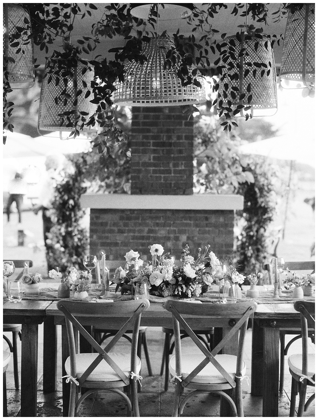black and white photo of table with centerpiece and hanging greenery from lights at del mar surf station, farmhouse table, budvases ,outdoor reception, medium sized centerpieces, romantic weddings, daisies, toffee roses, berries, cream flowers, white flowers, hydrangeas, majolica roses, explosion grass, outdoor wedding, covid wedding, san diego wedding florist, southern california elopement florist, socal florist, best wedding florist san diego ca, best wedding florist southern california, los angeles wedding florist, top rated wedding florist in california, del mar san diego, blush tapered candles, blush table runner, budvases